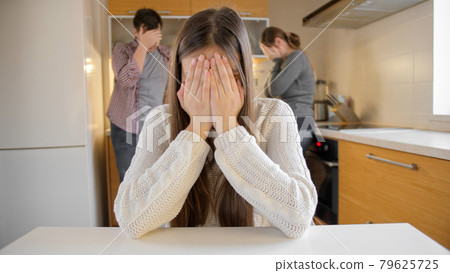 Upset girl crying and closing face with hands because on arguing and shouting parents on kitchen. Family violence, conflicts and relationship problems Upset girl crying and closing face with hands because on arguing and shouting parents on kitchen. Family violence, conflicts and relationship problems 79625725