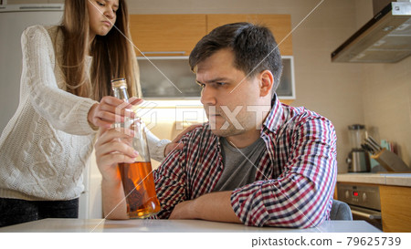 Angry teenage girl taking away bottle of alcohol from her drunk father drinking on kitchen. Alcoholism and addiction problems 79625739