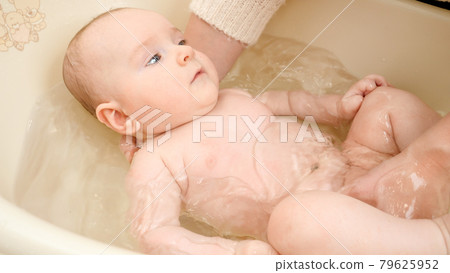 Cute baby looking at mother while washing in plastic bath. Concept of parenting ,baby care and healthcare. 79625952