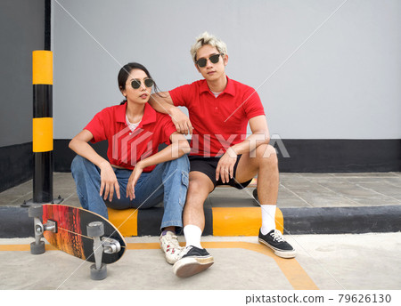 Asian couple resting after skateboarding. Young man in red T-shirt with collar and black sunglasses rest his arm at his girlfriend's shoulder. 79626130