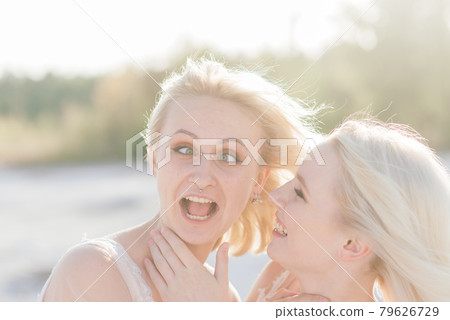 Beautiful lesbian couple walking on sand along river bank on their wedding day Beautiful lesbian couple walking on sand along river bank on their wedding day 79626729