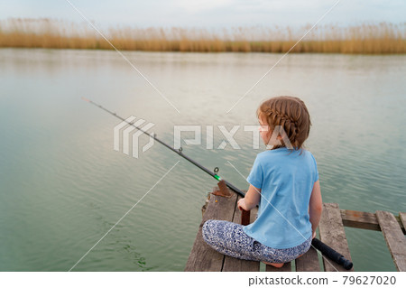 little girl sits on a wooden bridge on a river with fishing rod. little girl sits on a wooden bridge on a river with fishing rod. 79627020