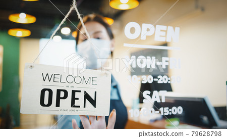 Asian female restaurant owner wear face mask, flip open sign at shop's door 79628798