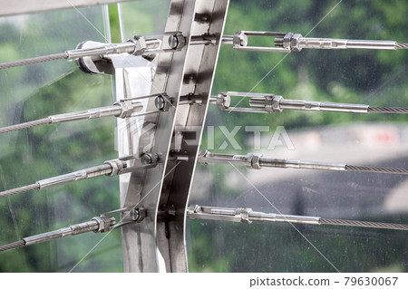 A close up view of tension steel cables with steel fasteners, a detail of frame on glass bridge with fastening engineering construction stainless steel turnbuckle. 79630067
