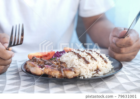young man eating grill chicken , rice and salad on plate on table  79631001