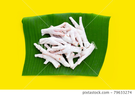 Raw chicken feet on banana leaf on yellow background. 79633274