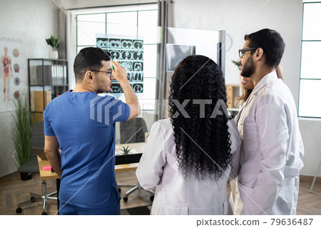 Four multiethnic doctors analyzing a scan or x-ray film or explaining a CT scan together Four multiethnic doctors analyzing a scan or x-ray film or explaining a CT scan together 79636487