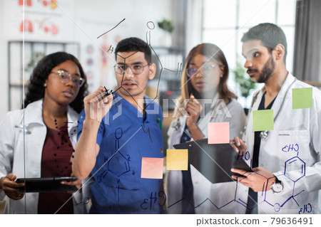 Team of doctors, discussing in front of glass wall, writing formulas, using notes and stickers Team of doctors, discussing in front of glass wall, writing formulas, using notes and stickers 79636491