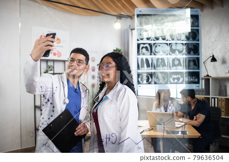 Multiracial doctors using smartphone for taking selfie near glass wall at office Multiracial doctors using smartphone for taking selfie near glass wall at office 79636504