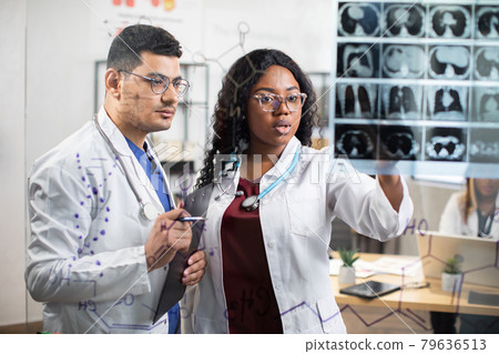 Group of young doctors, discussing in front of glass wall patient's diagnosis, looking at MRI scan Group of young doctors, discussing in front of glass wall patient's diagnosis, looking at MRI scan 79636513