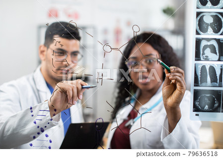 two multiracial scientists doctors, writing on the wall and looking at chemical formulas two multiracial scientists doctors, writing on the wall and looking at chemical formulas 79636518