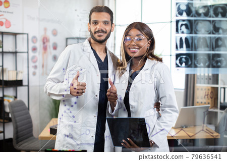 Indian and African medical doctors in uniform posing at camera indoors with thumbs up 79636541