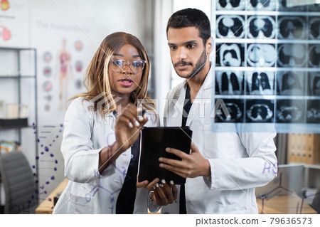 Multiracial doctors examining tomography of patient standing near glass wall Multiracial doctors examining tomography of patient standing near glass wall 79636573