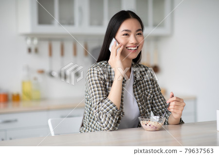 Beautiful young asian lady having breakfast and talking on phone Beautiful young asian lady having breakfast and talking on phone 79637563