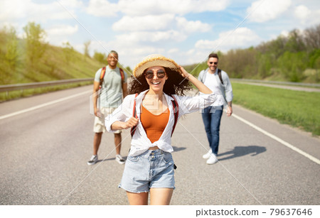 Beautiful young woman walking along highway with her male friends, having summertime journey, backpacking outdoors Beautiful young woman walking along highway with her male friends, having summertime journey, backpacking outdoors 79637646