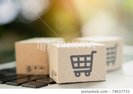 Shopping online. Cardboard box with a shopping cart logo on laptop keyboard. Shopping service on The online web. offers home delivery. copy space. Shopping online. Cardboard box with a shopping cart logo on laptop keyboard. Shopping service on The online web. offers home delivery. copy space. 79637732