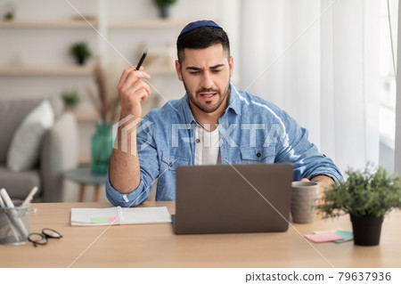 Focused israeli man working on laptop amd writing at home Focused israeli man working on laptop amd writing at home 79637936