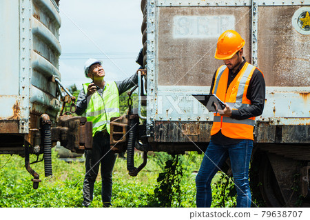 Inspector Engineering wearing helmet and vest worker unifrom checking railway construction work on rail track. Asian workers and coworkers stand beside old train bogies. 79638707