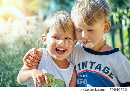 Boy hugs happy brother with toy car sitting on bench Boy hugs happy brother with toy car sitting on bench 79640710