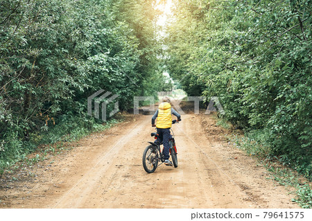 Boy in vest rides on modern bicycle on rural road 79641575