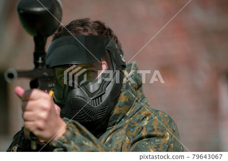 Portrait of young man with face mask and gun in the action game of paintball, simulate military combat using air guns to shoot capsules of paint at each other Portrait of young man with face mask and gun in the action game of paintball, simulate military combat using air guns to shoot capsules of paint at each other 79643067