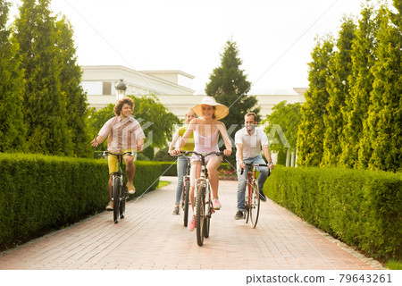 Happy friends riding bicycles on road in park. Happy friends riding bicycles on road in park. 79643261