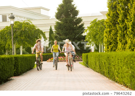 Happy students riding bicycles in summer park. Happy students riding bicycles in summer park. 79643262