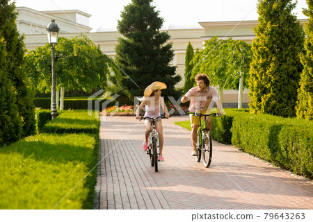 Cheerful couple riding bicycles in park. Cheerful couple riding bicycles in park. 79643263