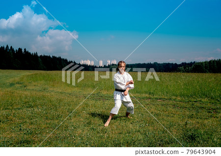 teenage girl training karate kata outdoors, prepares to perform downward block gedan barai in zenkutsu dachi stance 79643904
