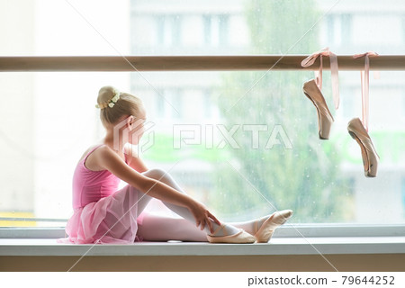 Ballerina in pink dress sitting on window-sill. Ballerina in pink dress sitting on window-sill. 79644252