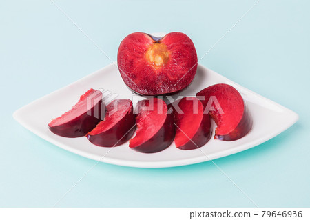 On a white saucer, a large plum, cut in half, with slices next to it. On a white saucer, a large plum, cut in half, with slices next to it. 79646936