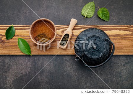 Black cast iron tea pot with herbal tea set up on dark stone background. Black cast iron tea pot with herbal tea set up on dark stone background. 79648233