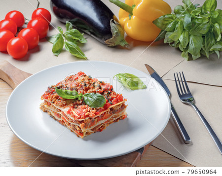 Piece of lasagna on white plate. Basil, tomatoes 79650964