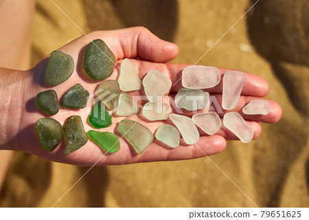 Pieces of sea glass are laid out on an open hand showing colours from green to white 79651625
