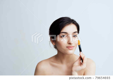pretty brunette applying makeup on face close-up naked shoulders 79654693