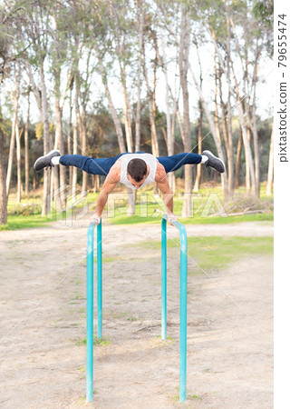 Male athlete exercising on parallel bars in forest. Male athlete exercising on parallel bars in forest. 79655474