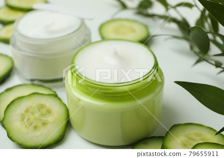 Jars with cosmetic cream, cucumber slices and branch on white table 79655911