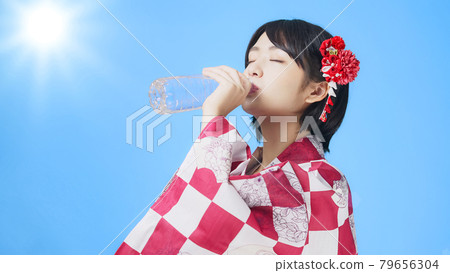 A woman in a yukata drinking water from a plastic bottle 79656304