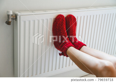 A young woman in warm, cozy knitted socks warms her legs by the 79659718