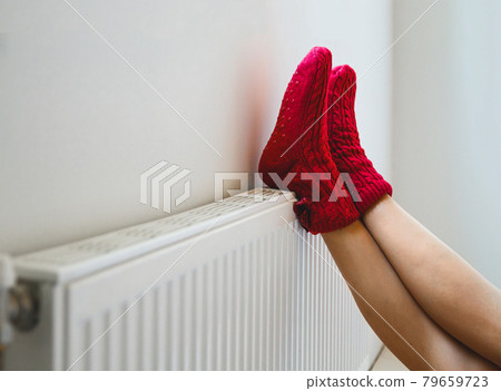 A young woman in warm, cozy knitted socks warms her legs by the 79659723