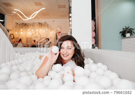 an attractive woman in white clothes lies in a dry pool with white balls. an attractive woman in white clothes lies in a dry pool with white balls. 79661882