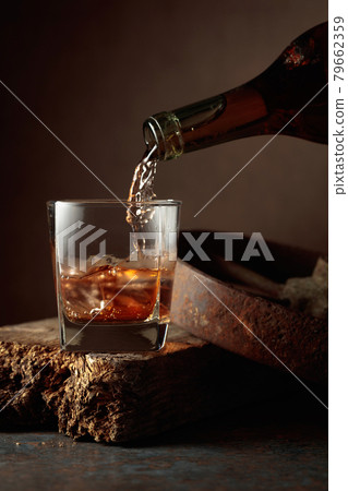 Whiskey is poured from a bottle into a frozen glass with natural ice. Whiskey is poured from a bottle into a frozen glass with natural ice. 79662359