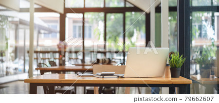 Close up view of co-working space table at cafe with laptop and blurry cafe interior in the background Close up view of co-working space table at cafe with laptop and blurry cafe interior in the background 79662607