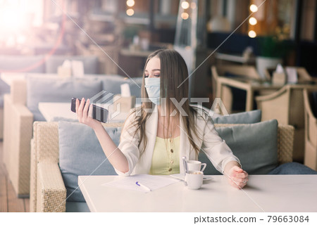 Serious woman with protective face mask looking at smart phone checking news on a cafe terrace 79663084