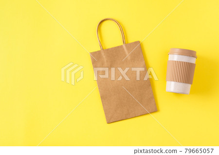 Mockup of kraft paper shopping bag with handles on yellow surface, reusable portable coffee mug for travel. Takeaway mug with spill stopper. 79665057