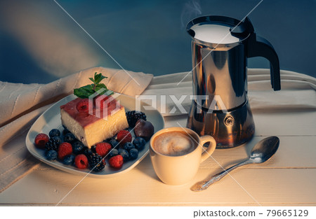 Breakfast still life - coffee pot, coffee and dessert with berries in jelly on top. Classic New York cheesecake slice with strawberries, raspberries, blueberries and chocolate on rustic 79665129