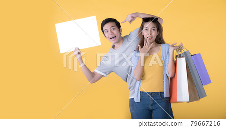 Asian couple holding blank billboard and shopping bags isolated on yellow background Asian couple holding blank billboard and shopping bags isolated on yellow background 79667216