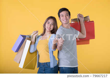 Asian couple holding credit card and shopping bags isolated on yellow background 79667217