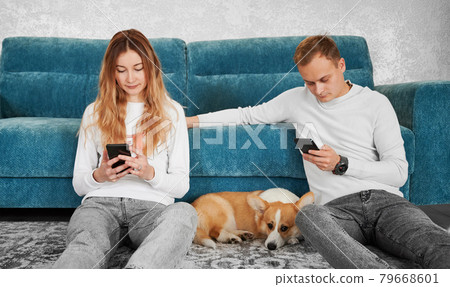 Beautiful couple sitting on the floor with dog and using cellphones. Beautiful couple sitting on the floor with dog and using cellphones. 79668601