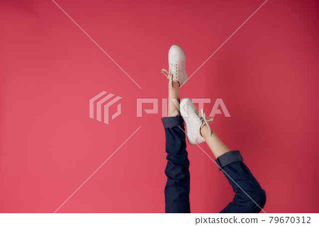 female legs in white sneakers upside-down view pink background fashion 79670312